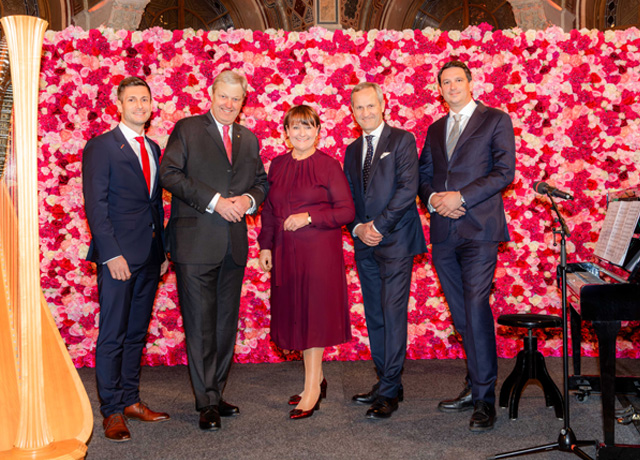 Fünf Personen, darunter Frau Herta Stockbauer, Herr Nikolaus Juhász und Dietmar Böckmann, stehen vor einer pinken Blumenwand und lächeln in die Kamera.