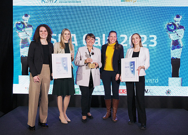 Fünf Frauen, darunter Frau Herta Stockbauer, stehen vor einer blauen Leinwand und zwei Frauen halten eine Urkunde in der Hand.