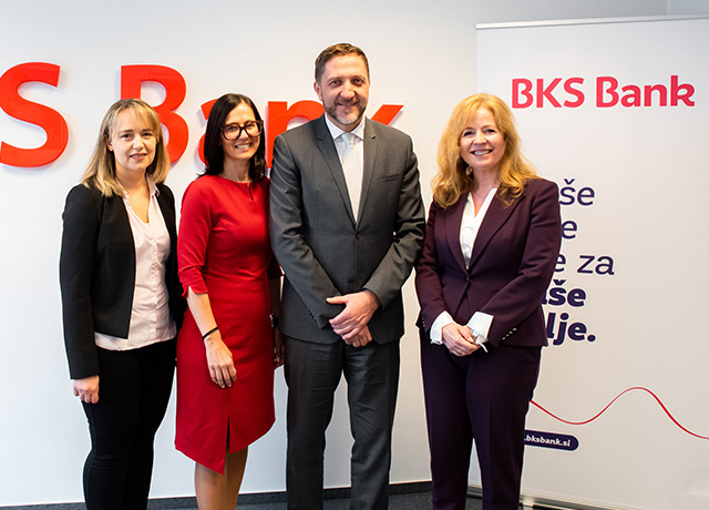 Vier Personen stehen in einer BKS Bank Filiale in Slowenien. Hinter ihnen ist das BKS Bank Logo zu sehen.