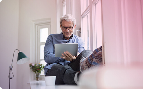 Mann sitzt zu Hause und schaut in sein Tablet