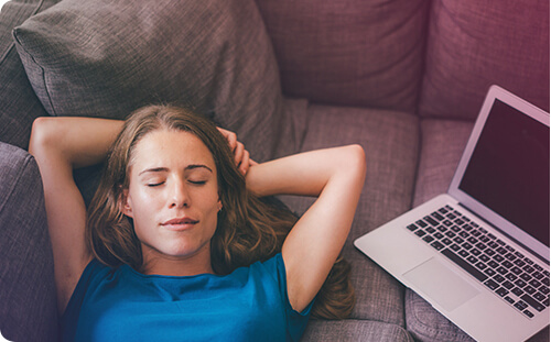 Frau liegt neben Laptop entspannt auf der Couch